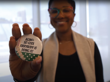 woman holding button that reads aging is so cool everyone is doing it